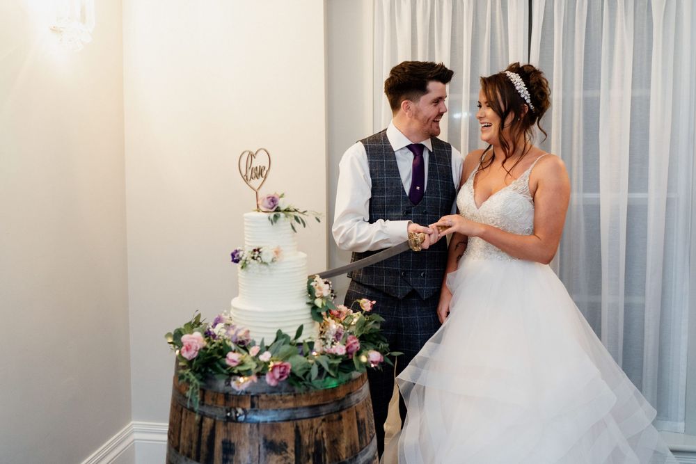 Newlyweds share a moment beside a rustic wine barrel decorated with floral arrangements.