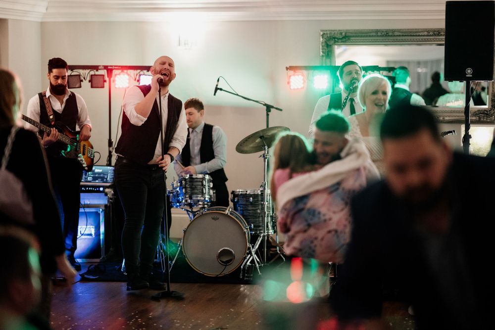 Live band performing at wedding reception with drum kit and colored lighting visible.