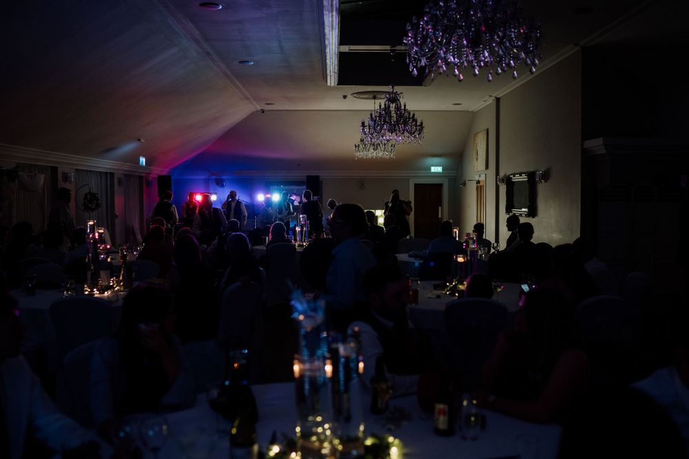 Dark reception venue with colored lighting and candle centerpieces creating ambiance.
