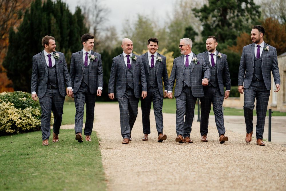 Wedding party in matching gray suits walking together on garden pathway.