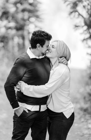 A romantic black and white portrait of a couple embracing outdoors with a soft, blurred background.