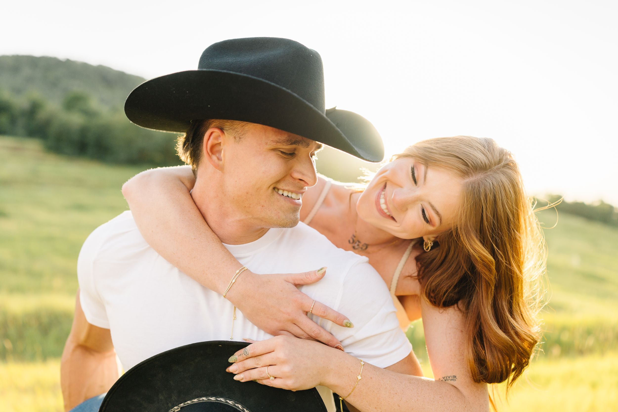 Couple embracing in sunset field with cowboy hat for romantic photo.