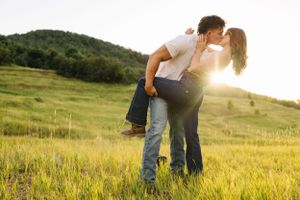 A couple shares an intimate moment in a sunlit meadow during golden hour.