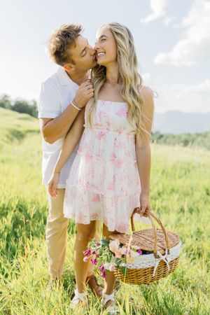 Romantic countryside photoshoot with couple and picnic basket in flowering meadow.