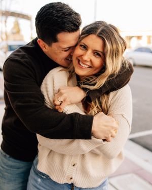 A joyful couple embraces and laughs together while wearing cozy sweaters outdoors.