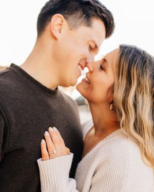 Romantic couple in casual sweaters share an intimate moment while showing off engagement ring.