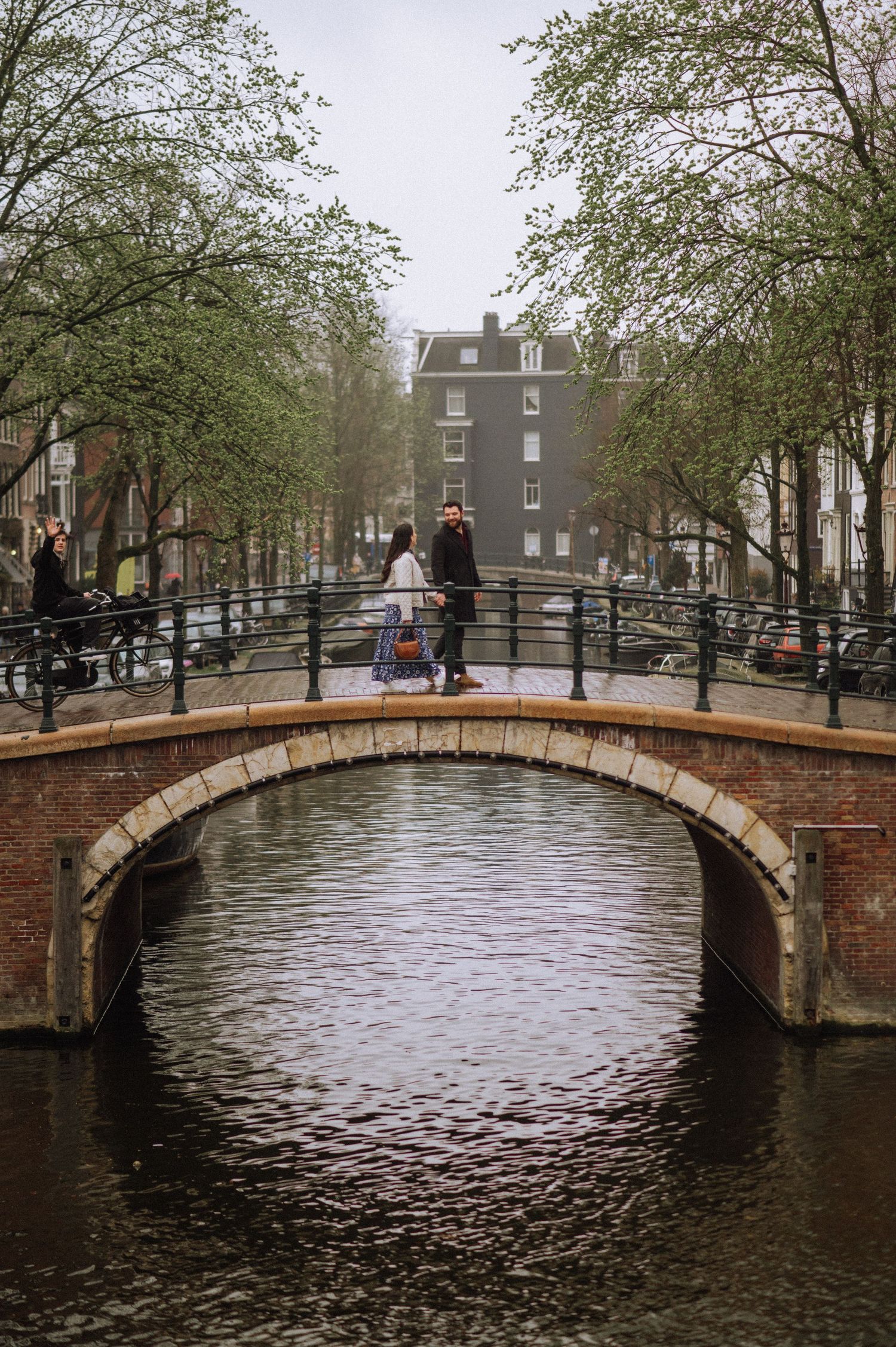 Stone arch bridge over Amsterdam canal with trees and buildings in background.