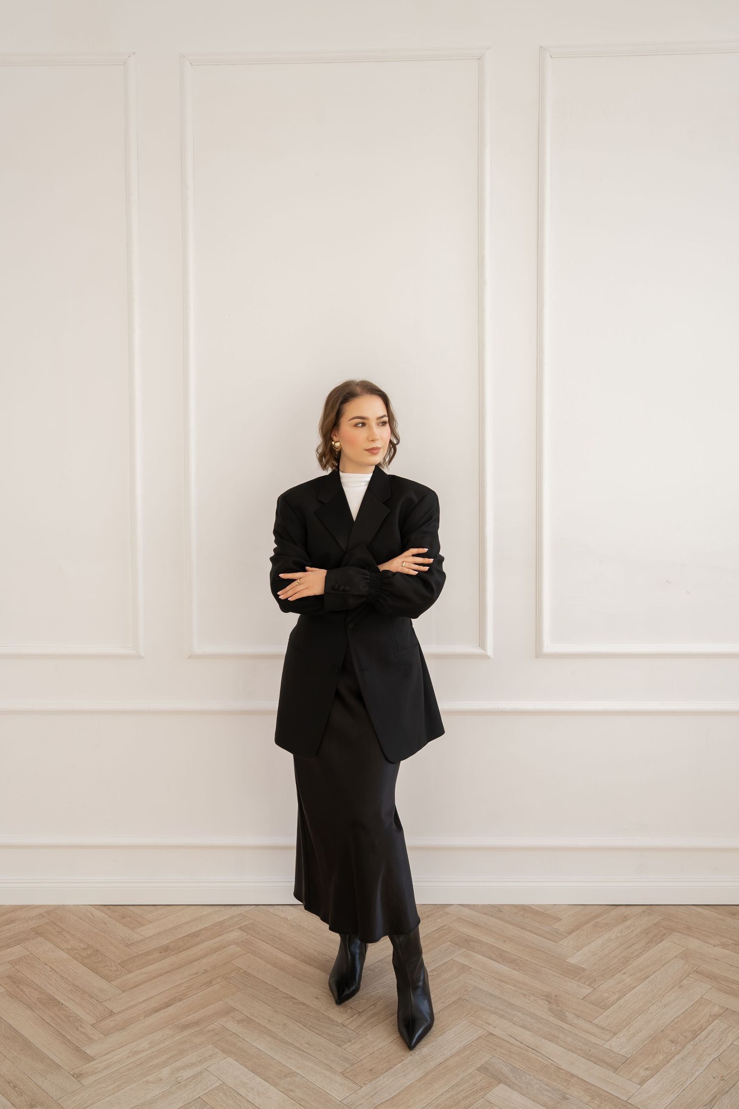 Professional woman in black business attire standing against white paneled wall.
