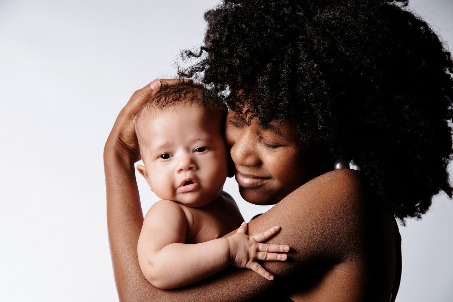 Dunkelhäutige Frau hält ihr Baby beschützend im Fotostudio, Hand über dem Kopf- liebevolles Bauch- Baby-Bengel Portrait