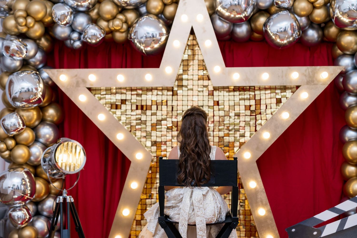 Jeune fille bat mitzvah assise devant une grande étoile lumineuse dorée, décor festif et glamour.