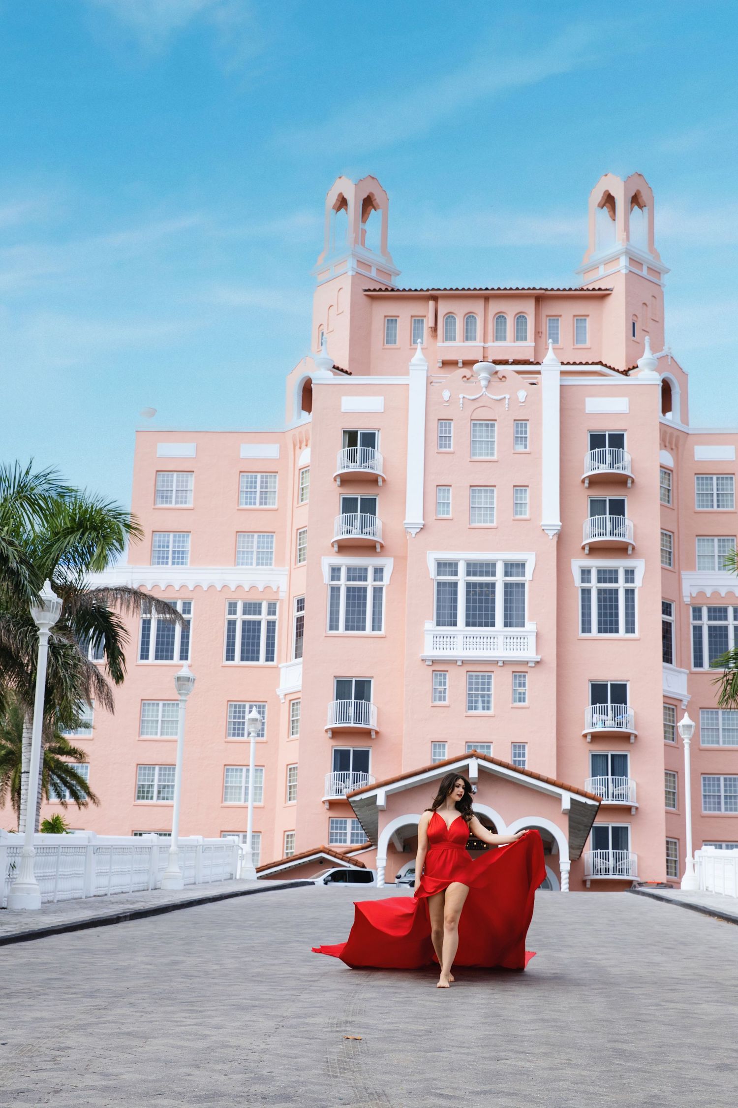Flying Dress. A pink art deco hotel building with palm trees and a person in a flowing red dress moving across the frame in multiple shots.