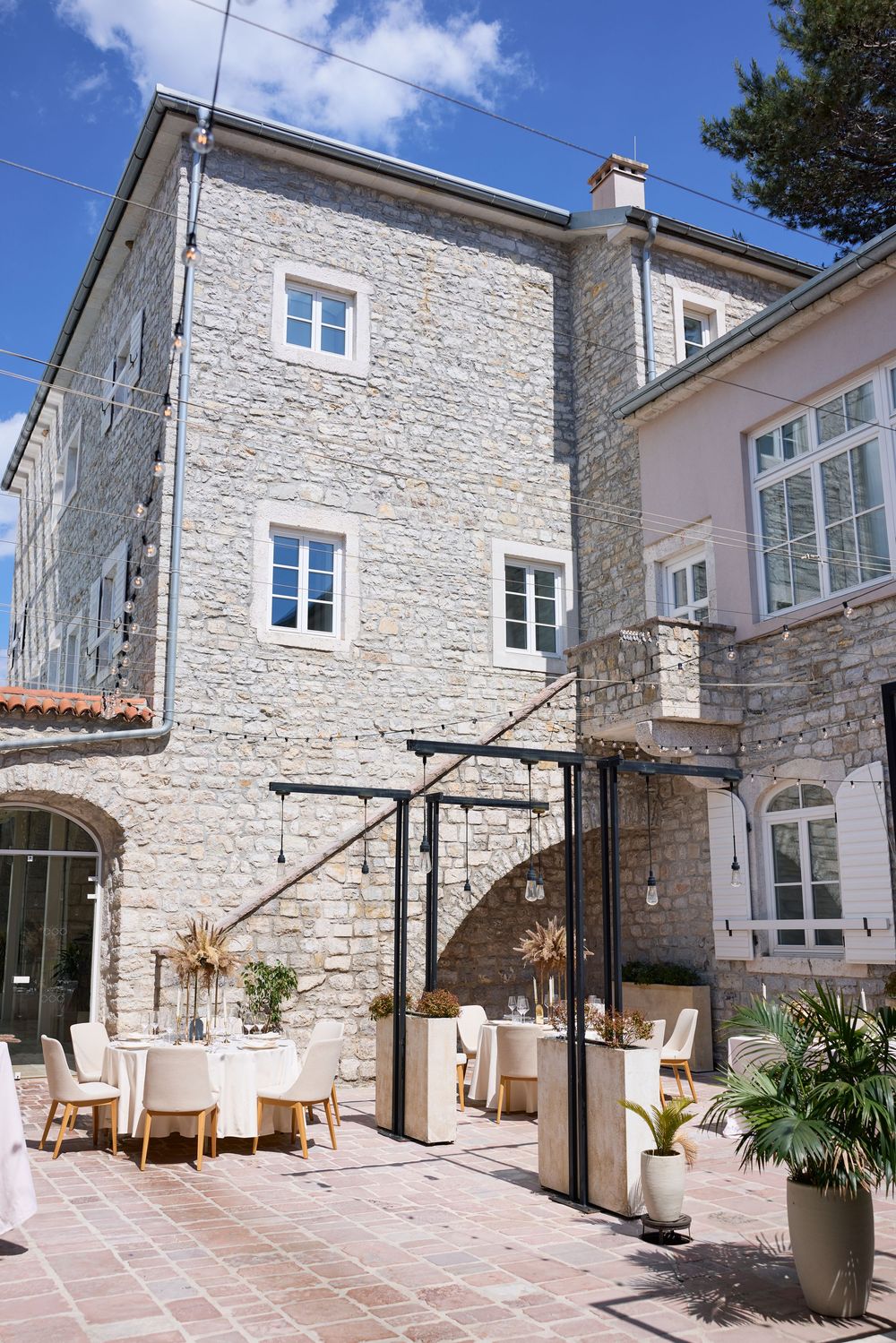 Mediterranean-style courtyard with stone walls and elegant outdoor dining setup under blue skies.