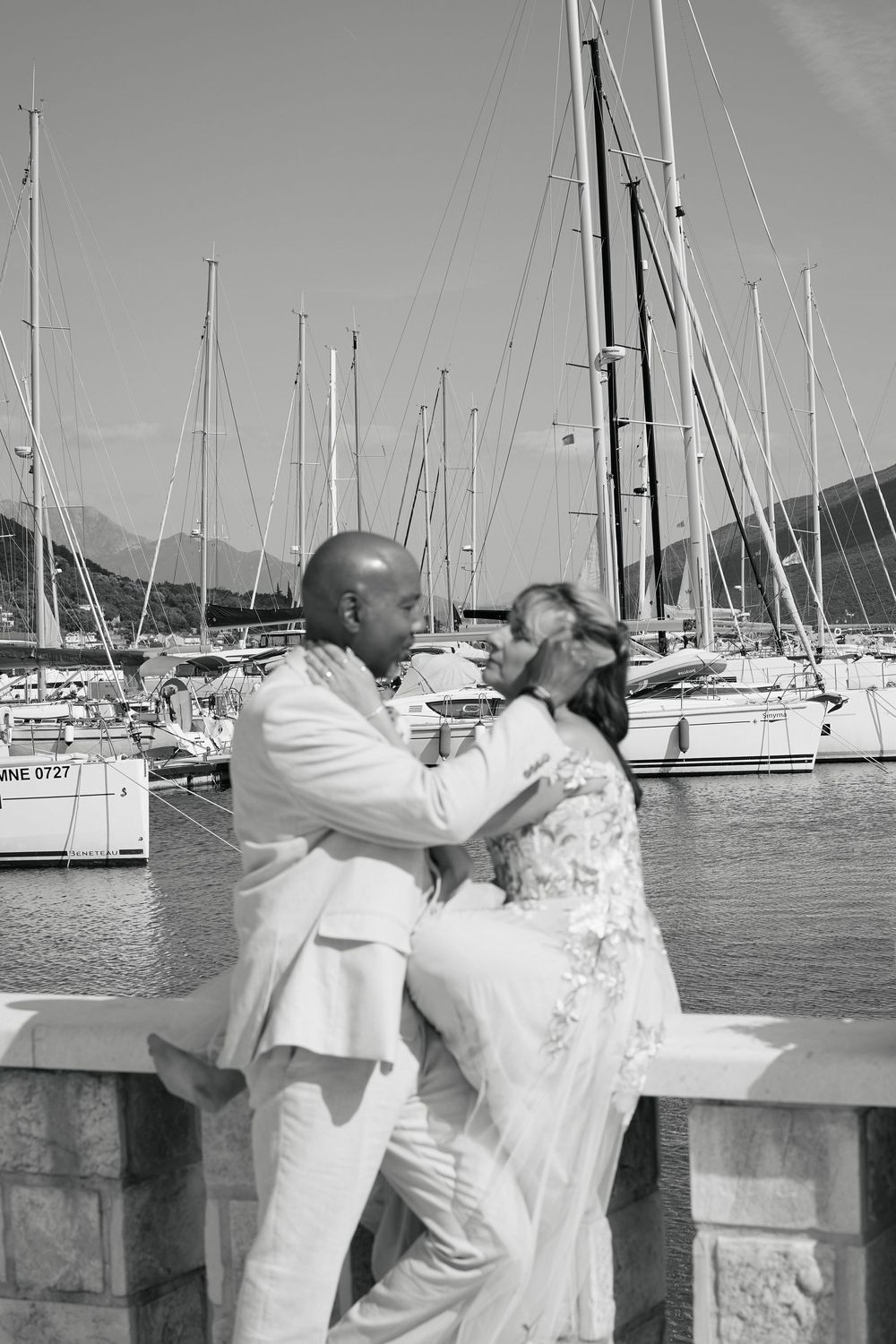 Wedding couple sharing romantic moments by a marina with sailboats in the background.