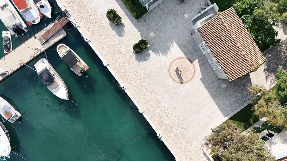 Overhead drone shot of boats docked at a marina with clear turquoise waters and concrete piers.
