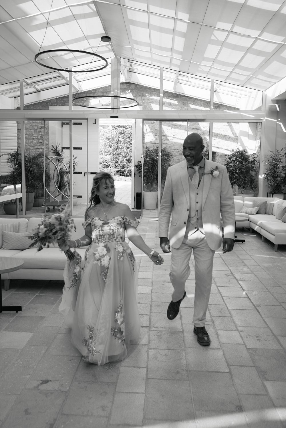 Black and white photo of couple walking through sunlit conservatory space.