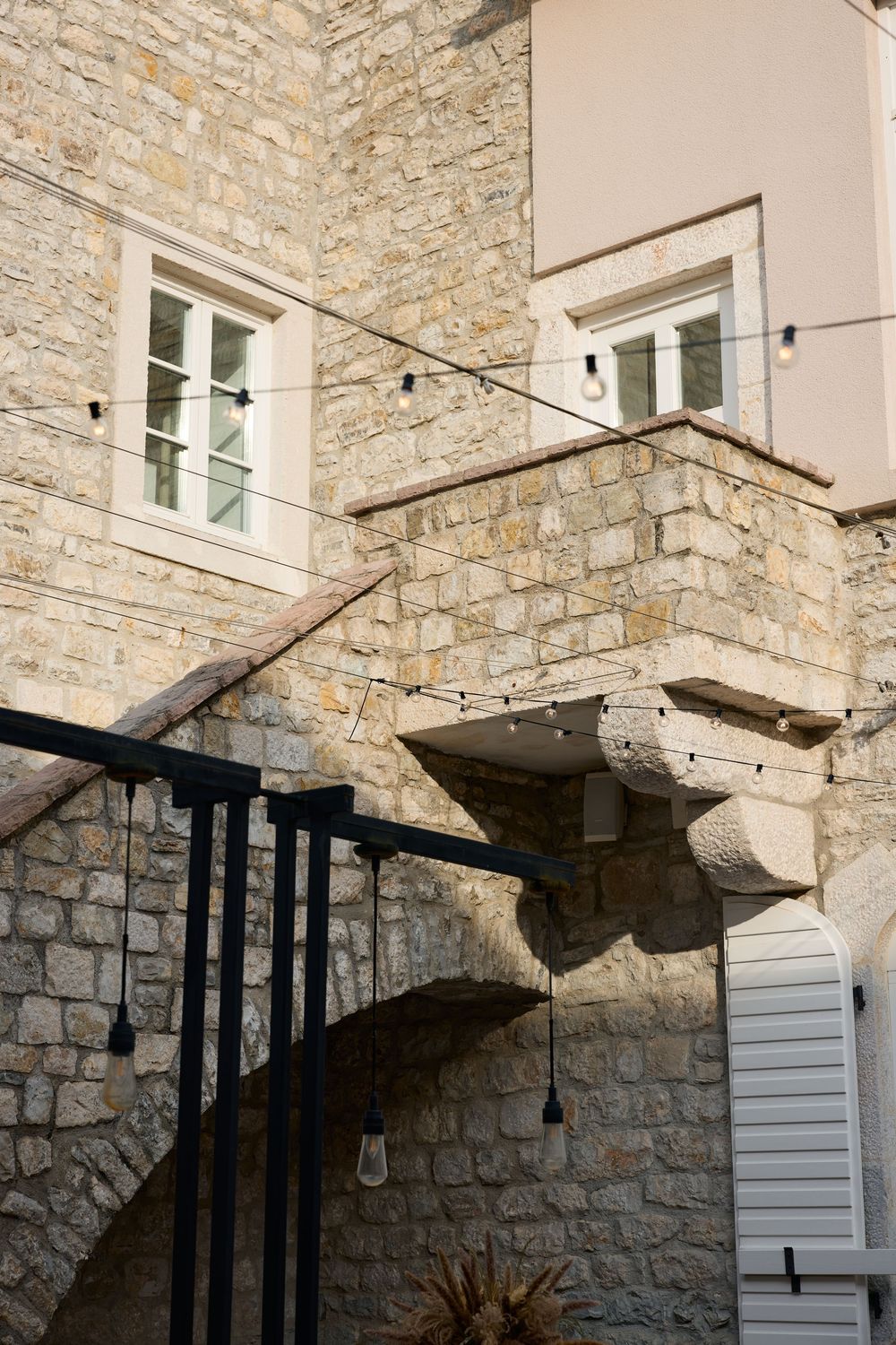 Stone building exterior with white windows and string lights hanging from rustic architectural details.