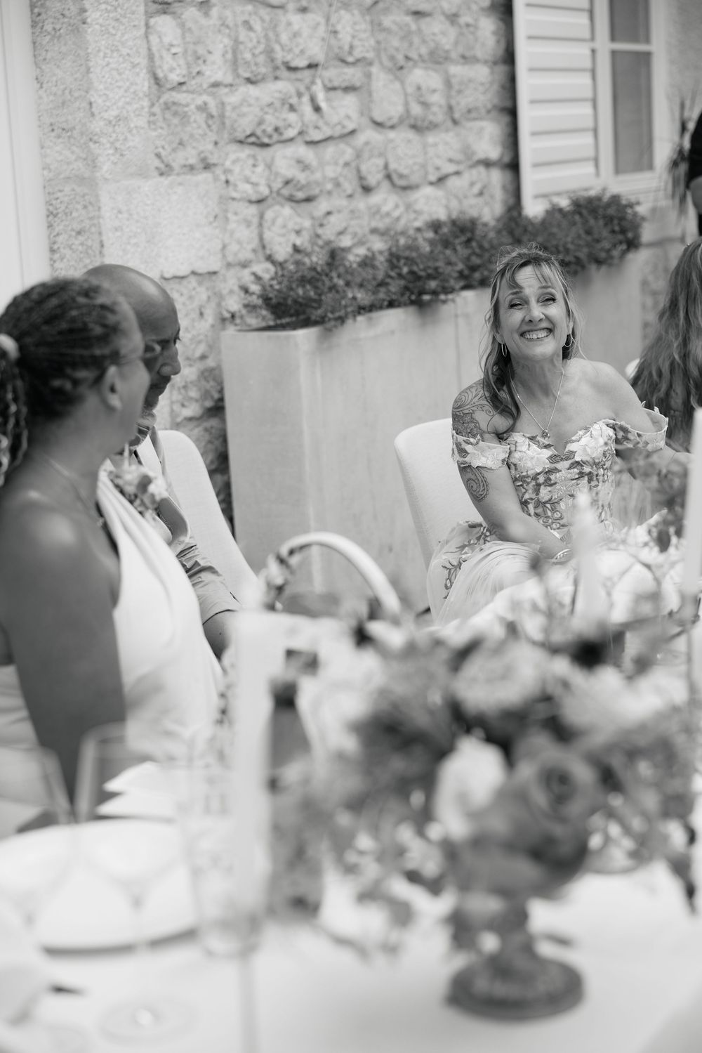 Elegant wedding reception table setup with floral centerpieces and white decor against a stone wall backdrop.