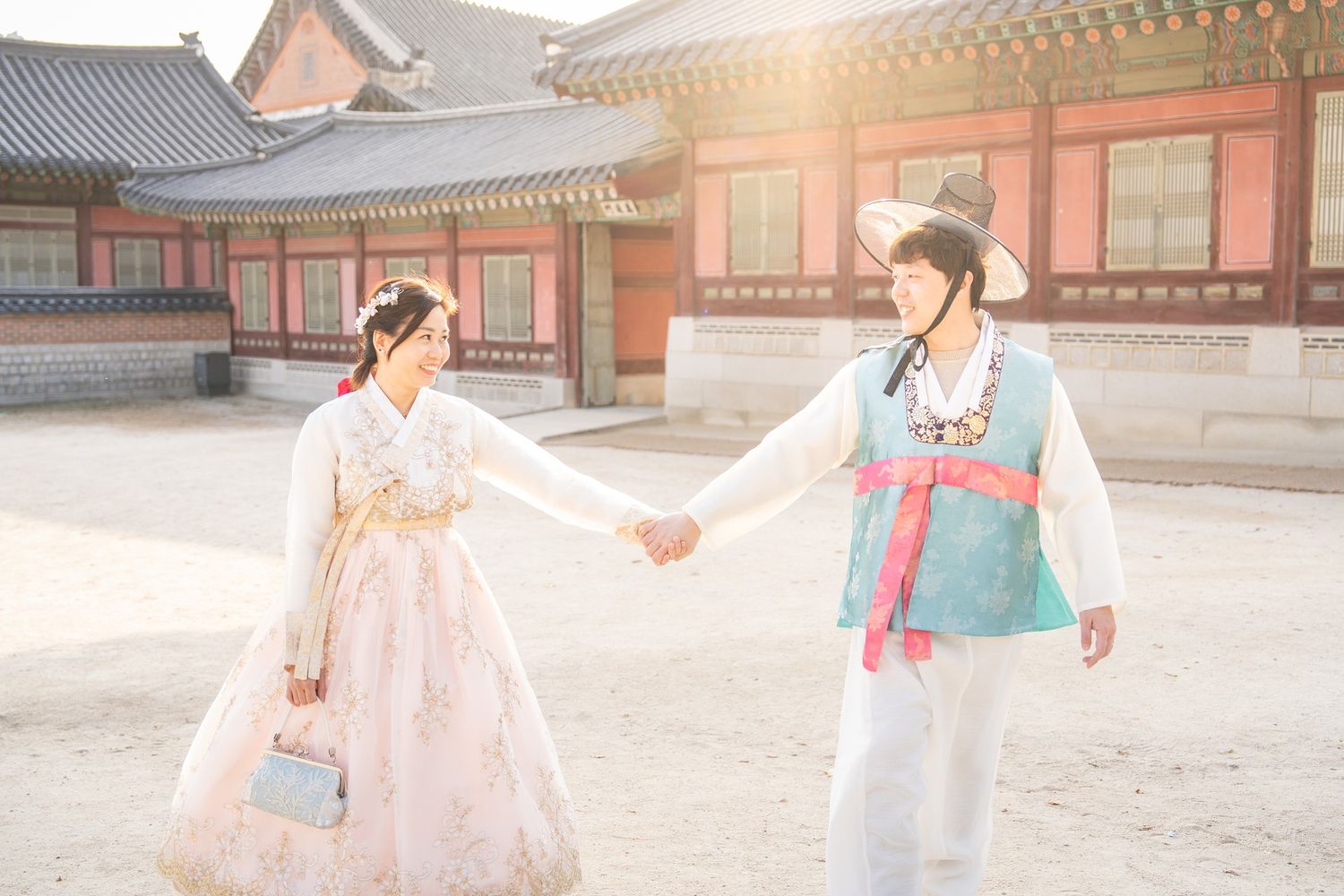 People wearing traditional Korean hanbok clothing walk through a historic palace courtyard in Seoul.