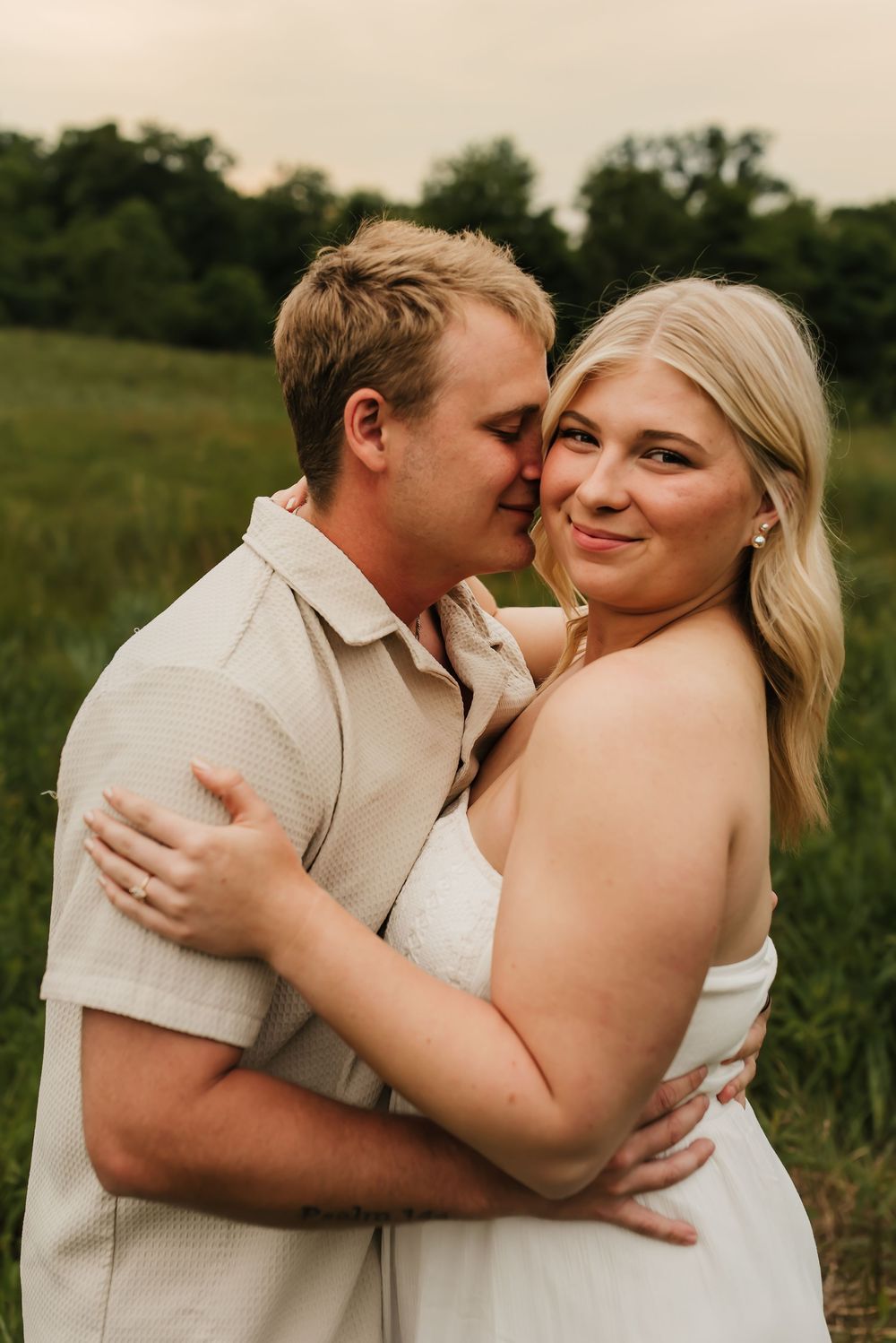 Romantic engagement photo of couple cuddling in soft golden hour light.