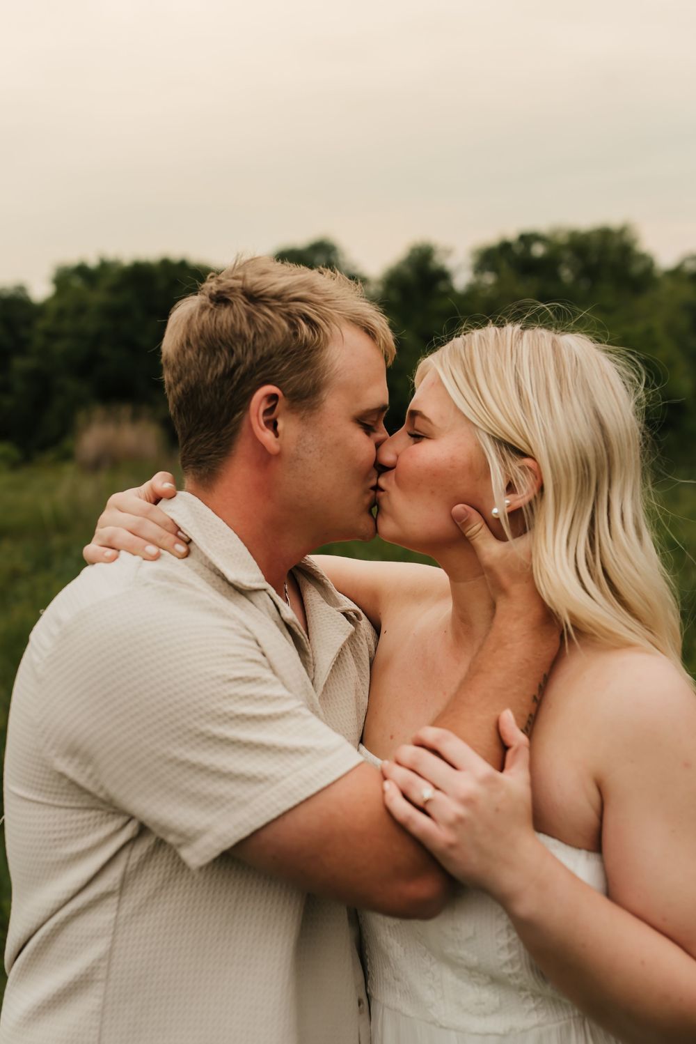 Romantic engagement photo of couple cuddling in soft golden hour light.