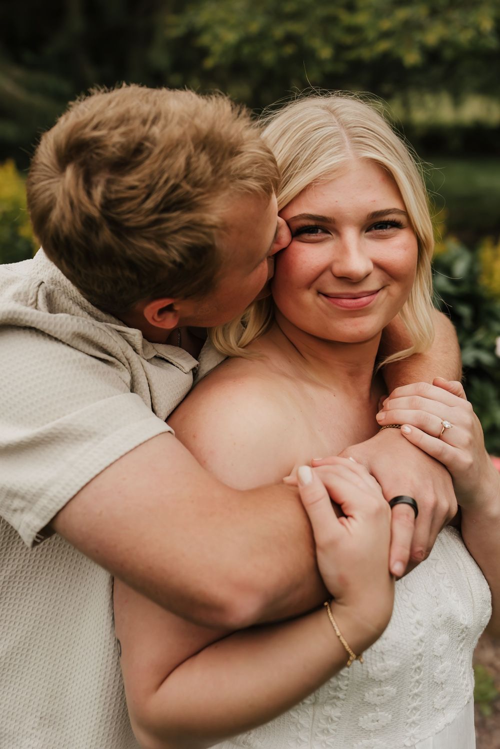 Engaged couple embracing in a sunlit field during an outdoor engagement session.