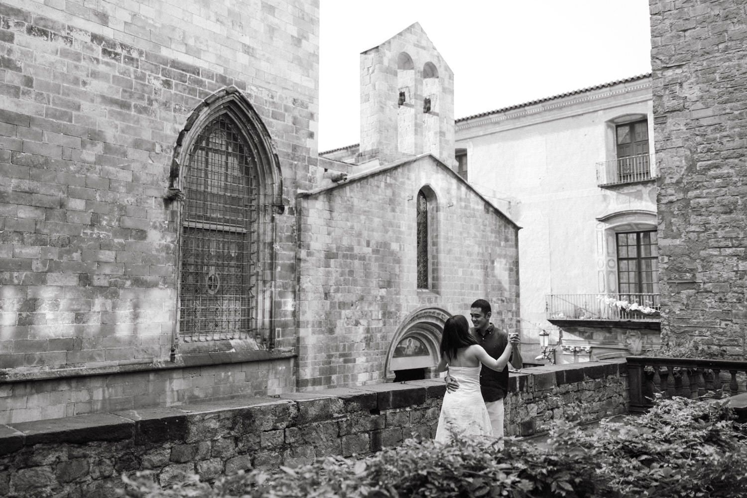 Couple walking playfully through historic stone alleyway in black and white.
