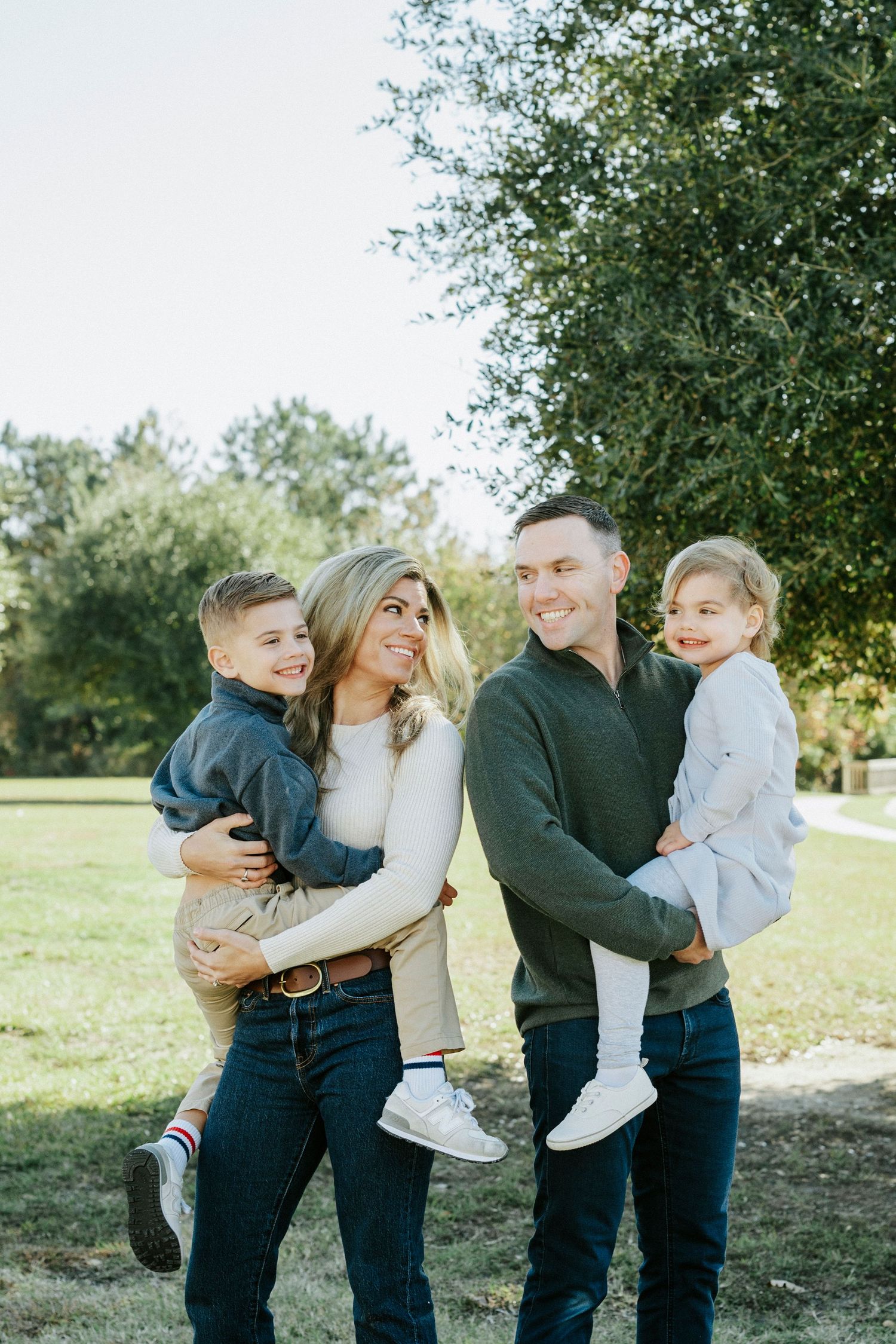A family of four wearing coordinating navy and white outfits poses together outdoors in a natural setting.