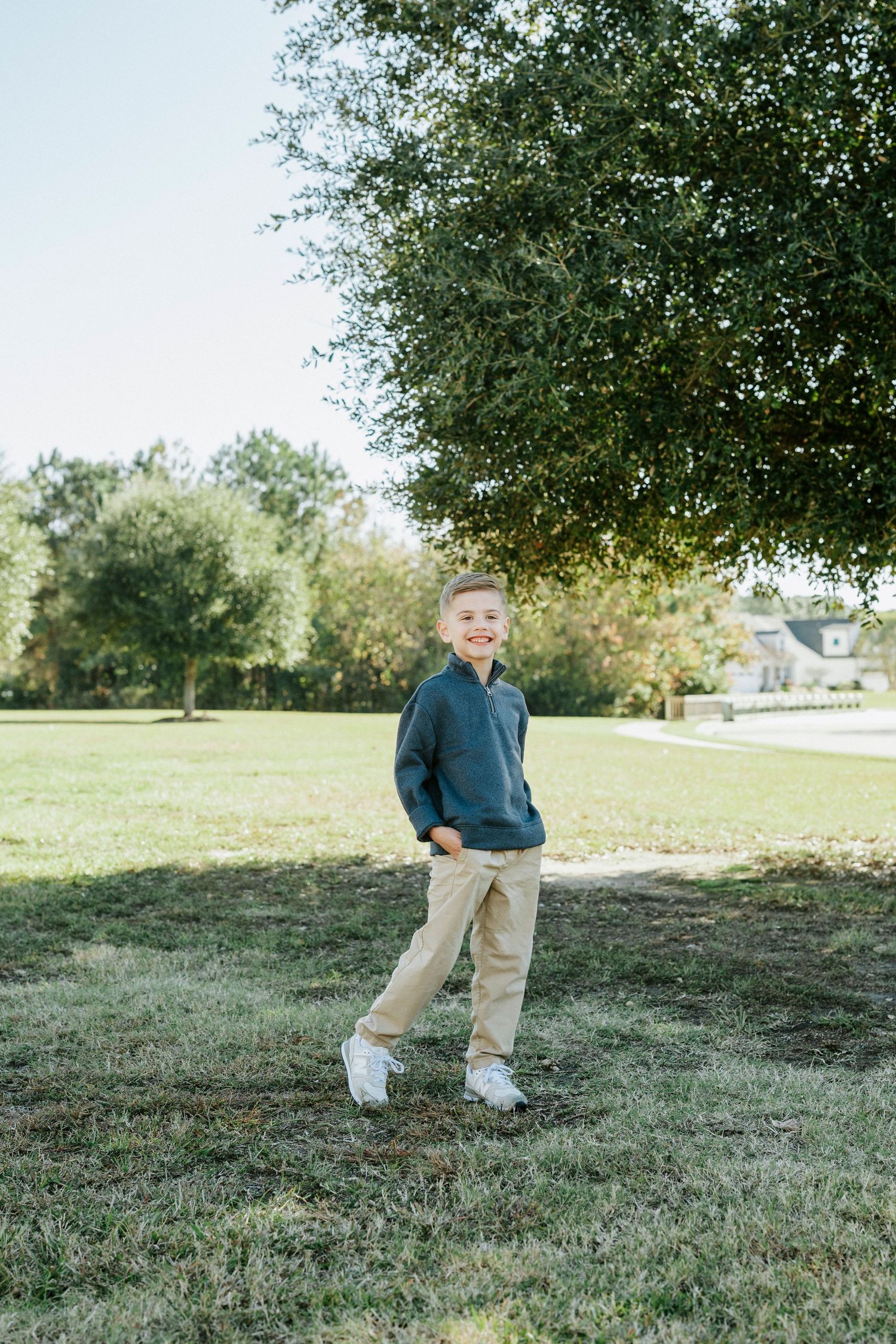 A small child wearing khaki pants and a blue sweater plays and runs in a grassy field on a sunny autumn day.