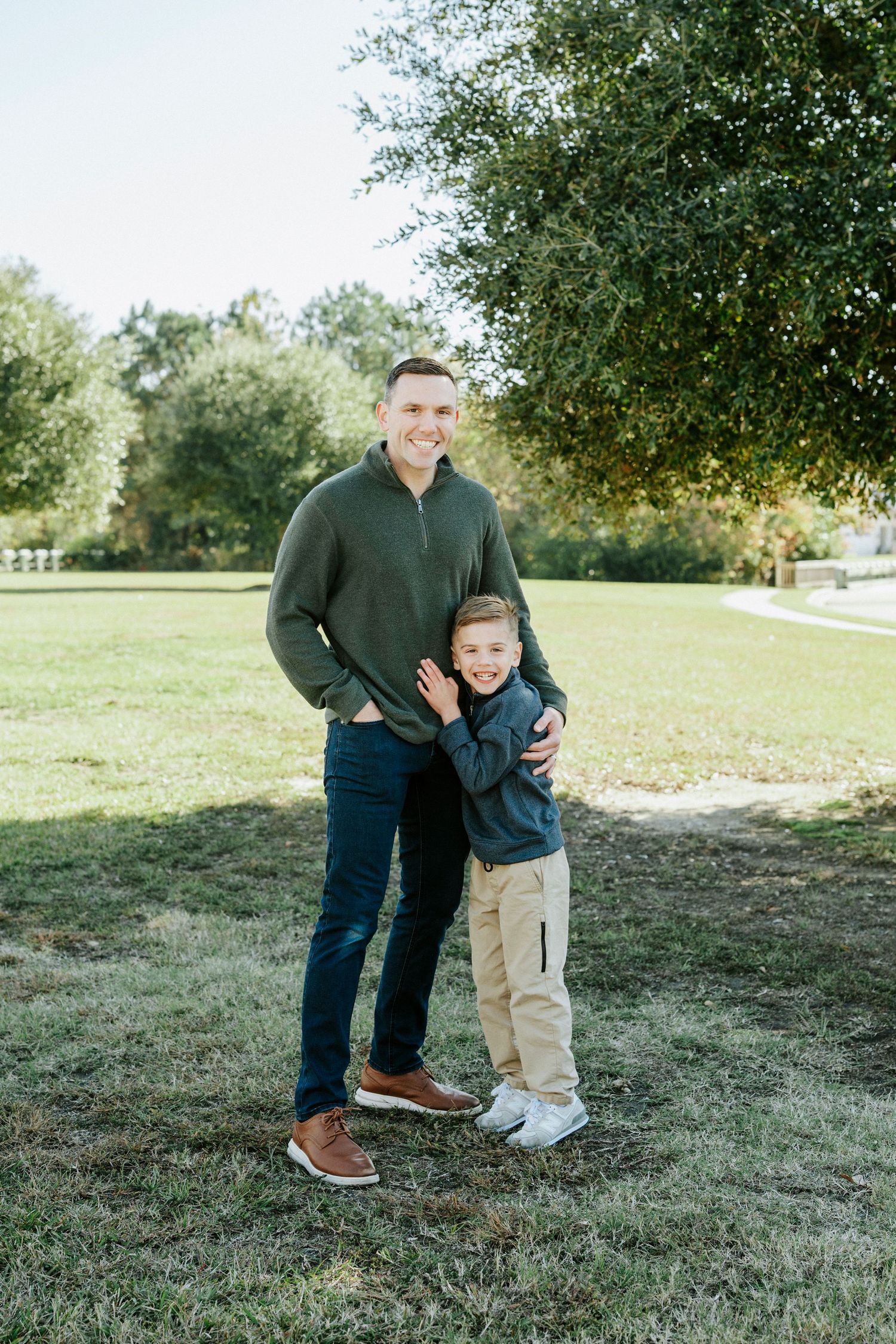 A tender outdoor moment captured in a grassy field with casual fall attire and warm natural lighting.