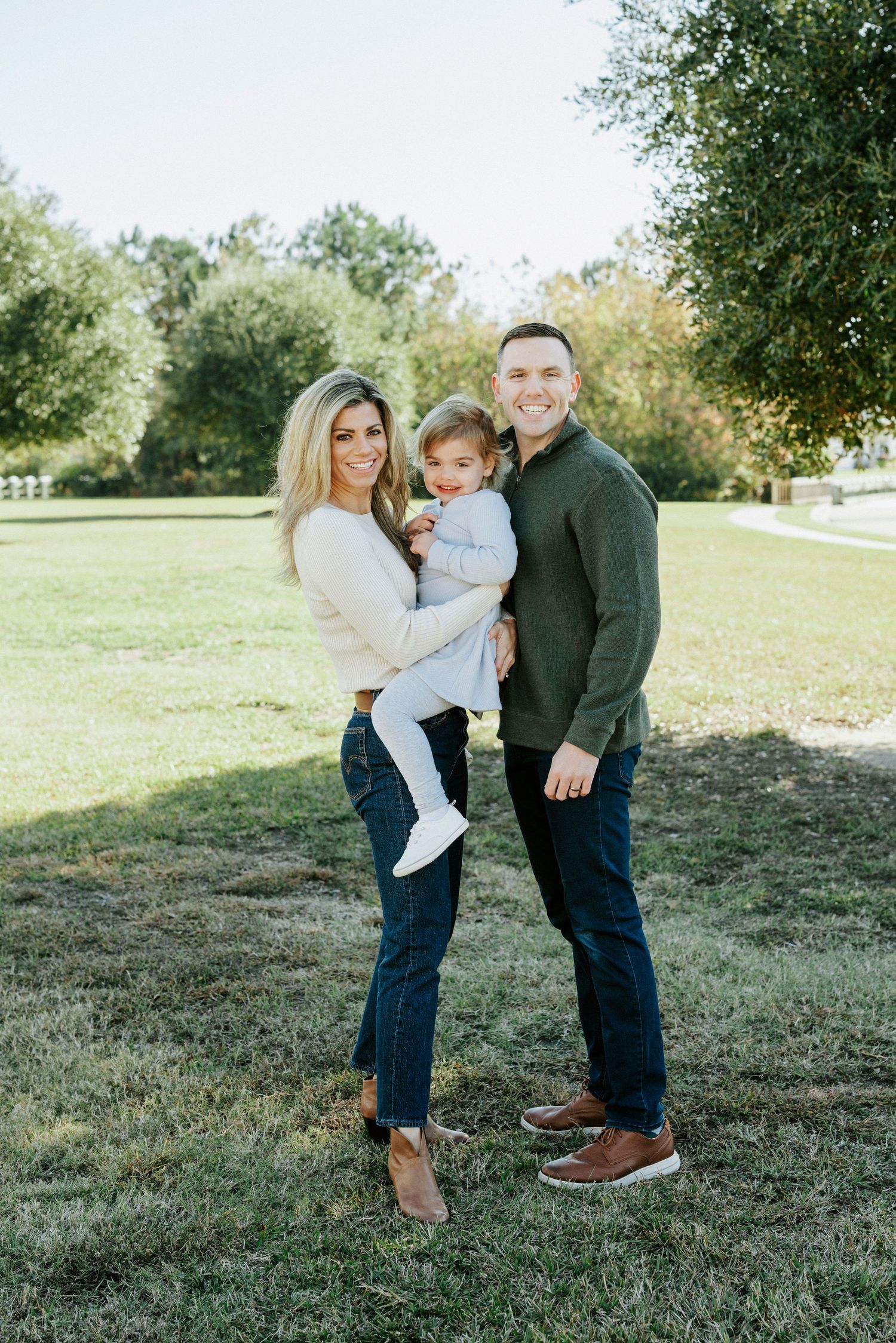 A family shares a tender moment together on grassy terrain under trees during an outdoor photo session.