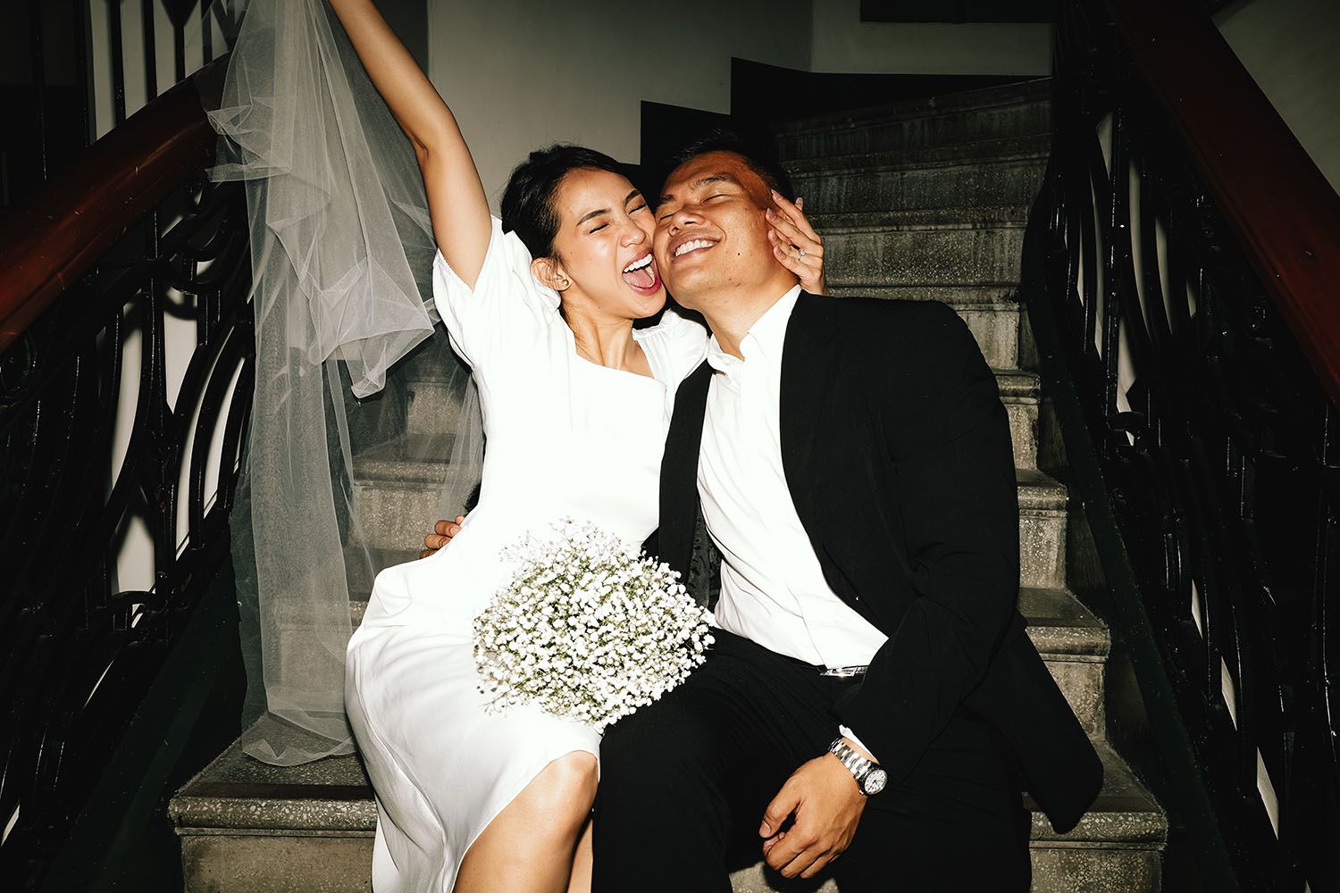 A couple in formal attire descends a dark staircase feeling happy