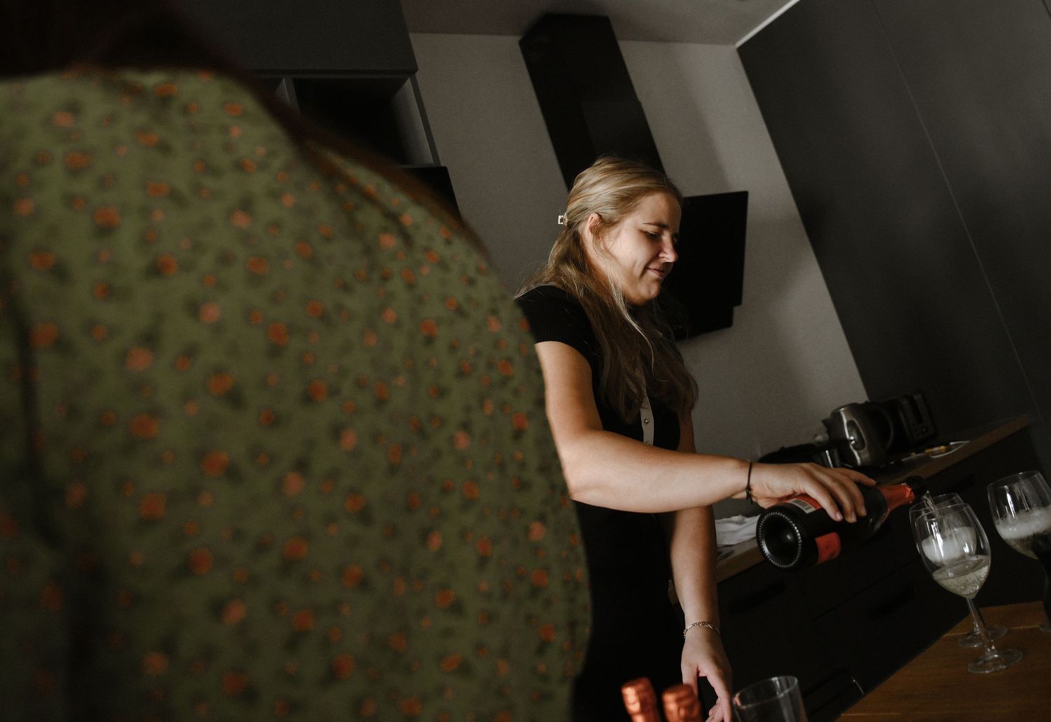 Photographer adjusts camera settings in a dimly lit studio with floral wallpaper background.