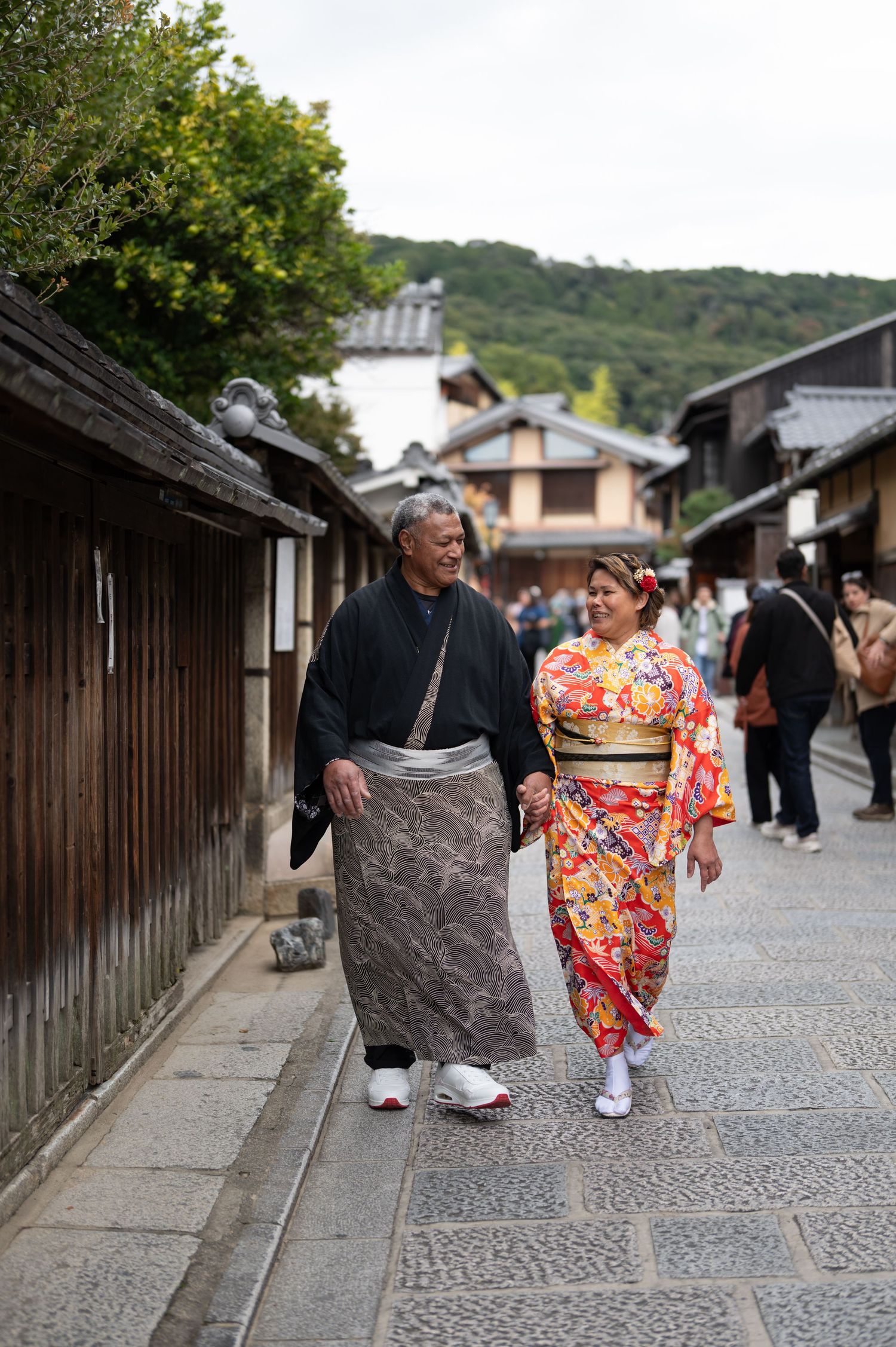 Couple dressed in traditional Japanese kimono walk together along scenic Kyoto cobblestone street.