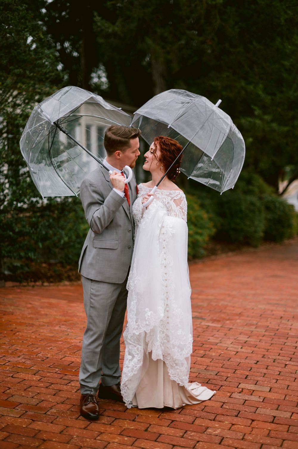 A romantic wedding couple shares intimate moments under a flowing veil on a red brick pathway.