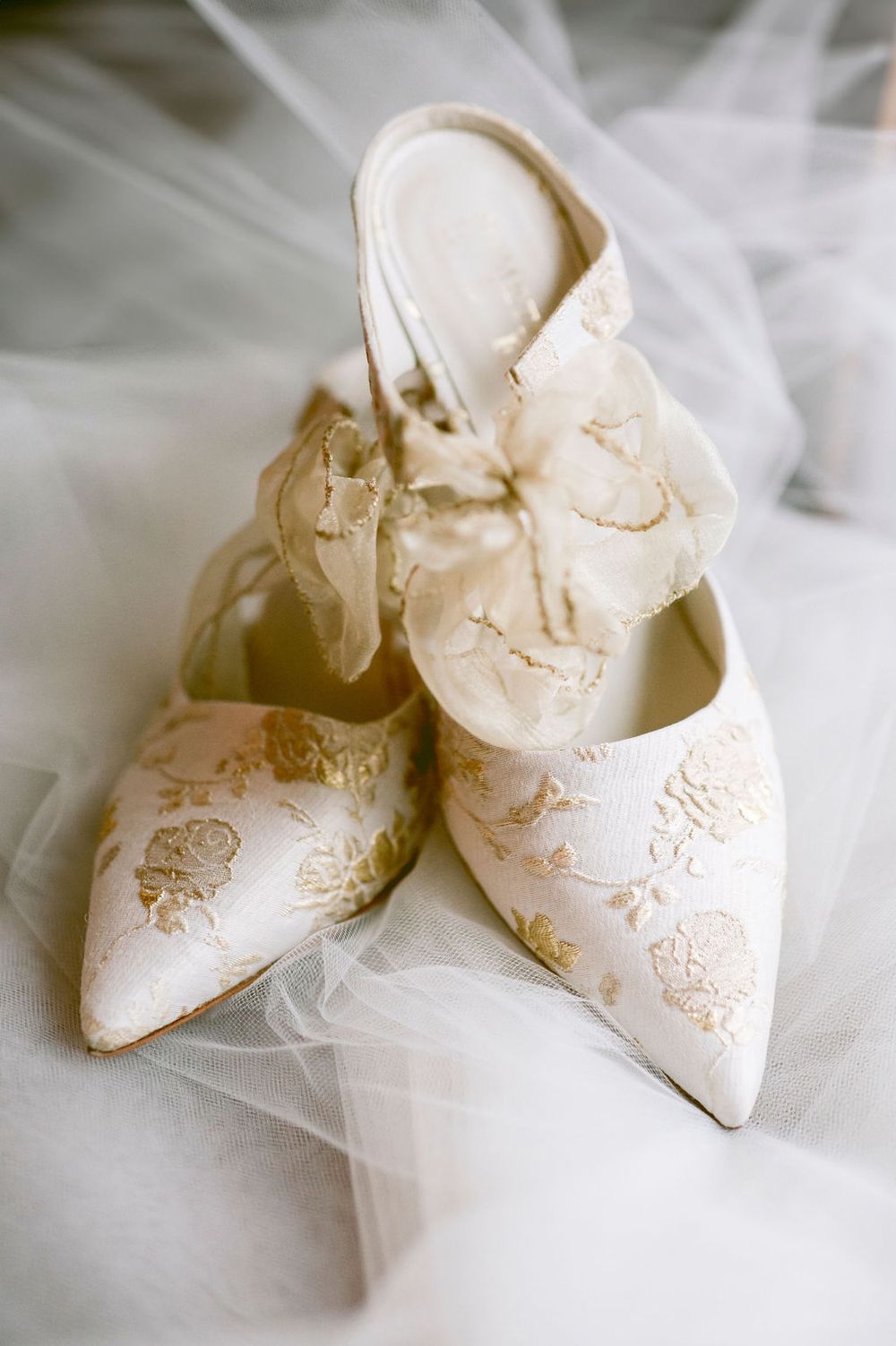 Elegant white vintage bridal shoes with delicate lace embroidery details resting on soft tulle fabric.