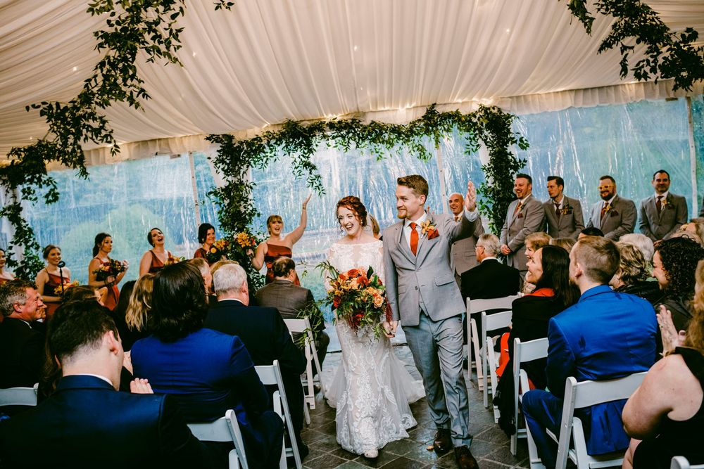 Wedding guests dance and celebrate together under a white draped tent ceiling during an evening reception.
