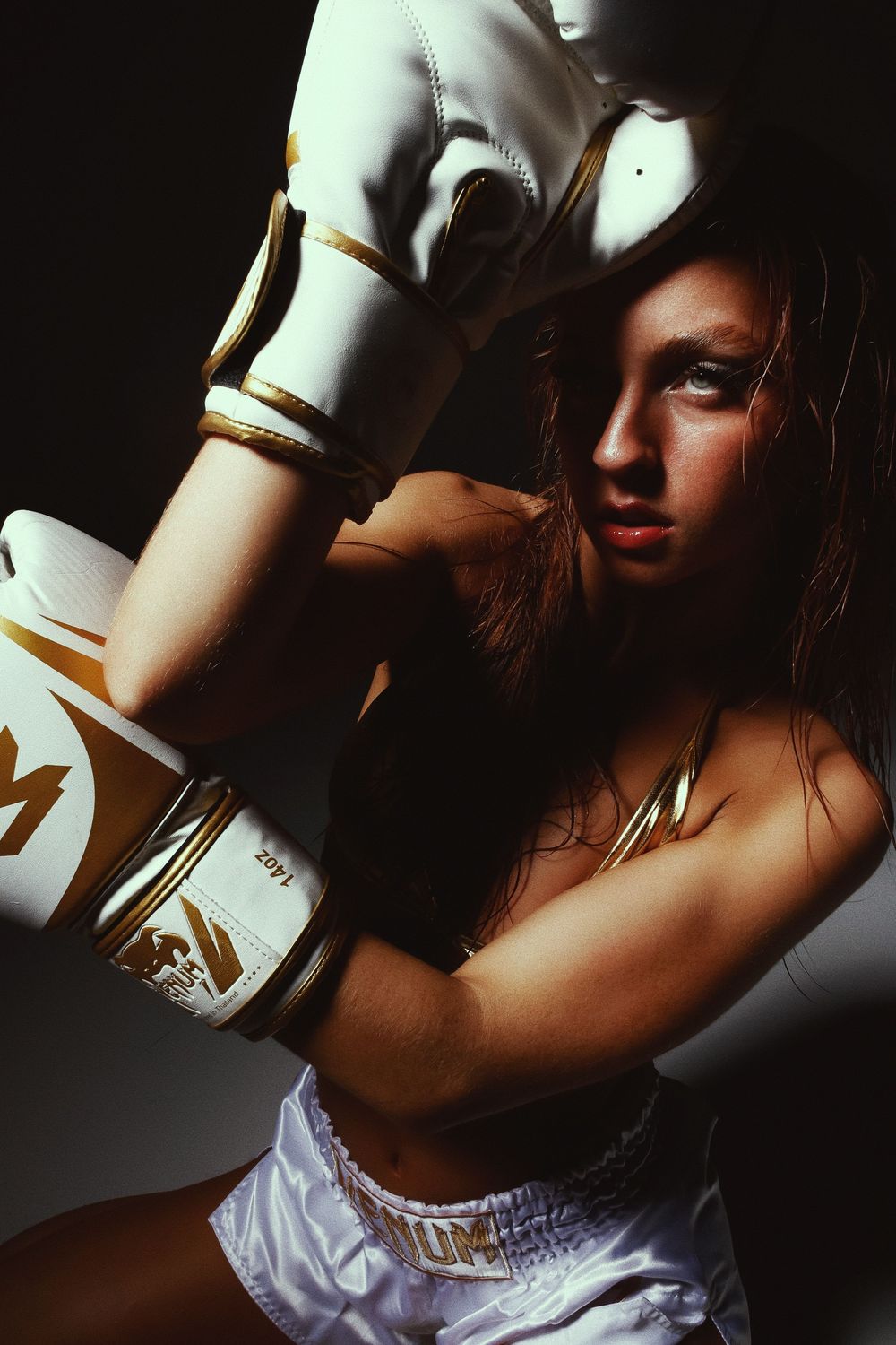 Dramatic low-key portrait of a boxer wearing white gloves and shorts in moody lighting against dark background.