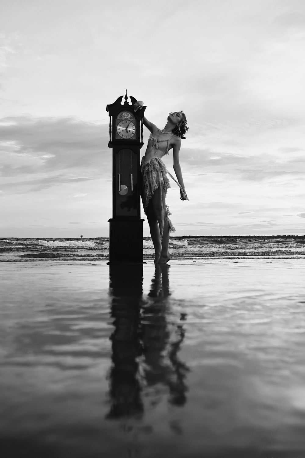 A dramatic black and white series showing a figure and vintage clock standing in shallow ocean waters at sunset.