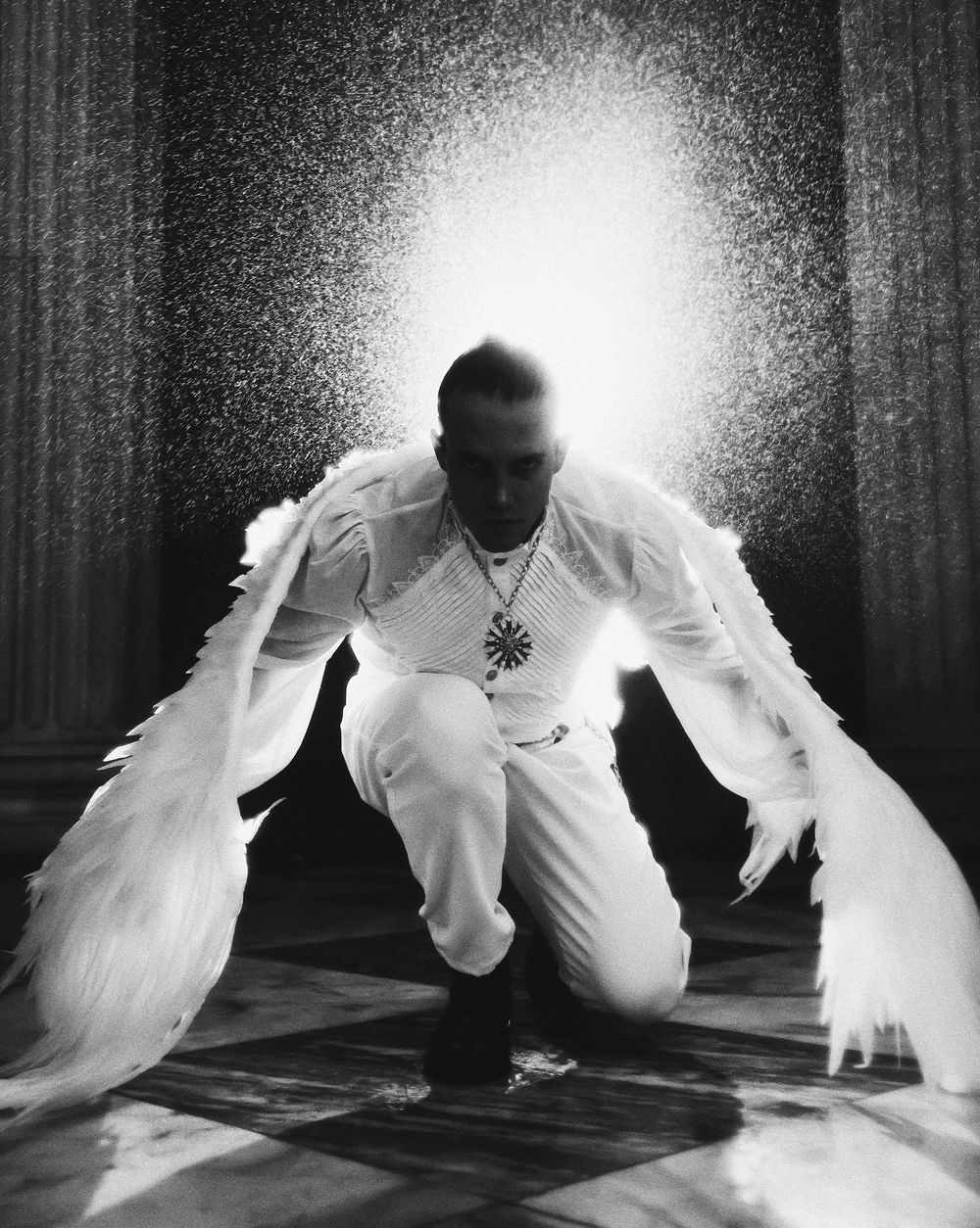 A dramatic black and white photo sequence shows a figure with white wings moving across a dark floor in four stages.