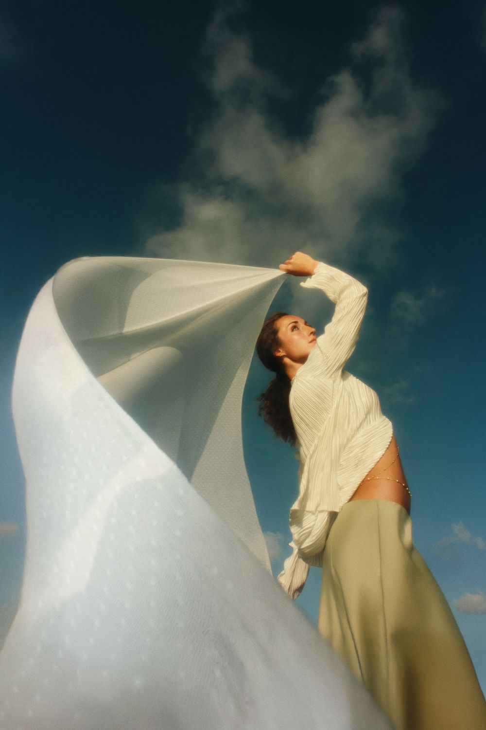A figure in a flowing white dress moves gracefully against a dramatic cloudy sky in a series of artistic poses.