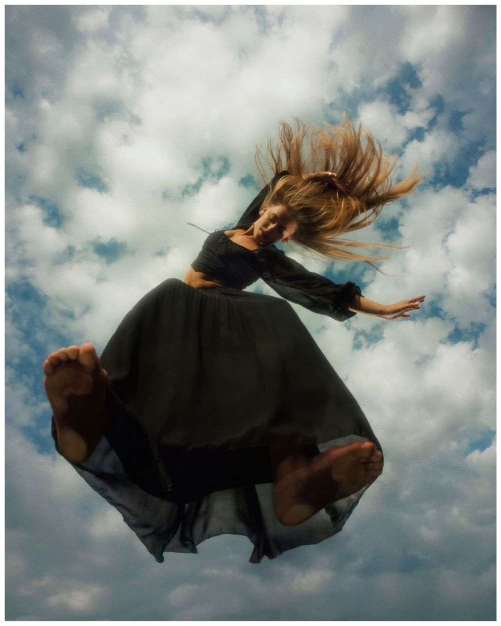 A figure in a black dress floats gracefully through the cloudy sky in a series of dynamic levitating poses.