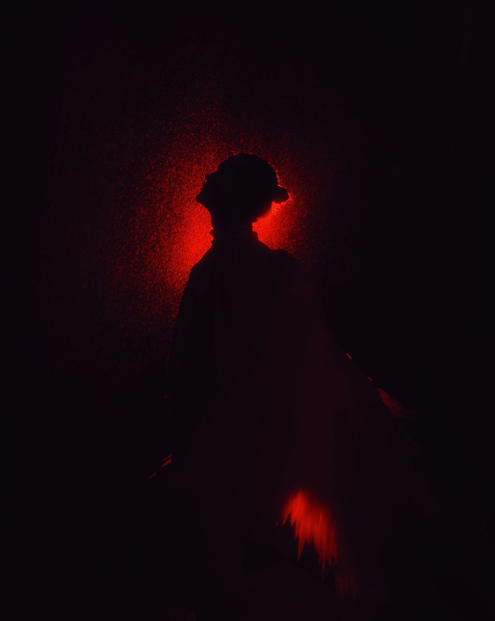 Dramatic silhouette of a figure against a dark background illuminated by an eerie red glow.
