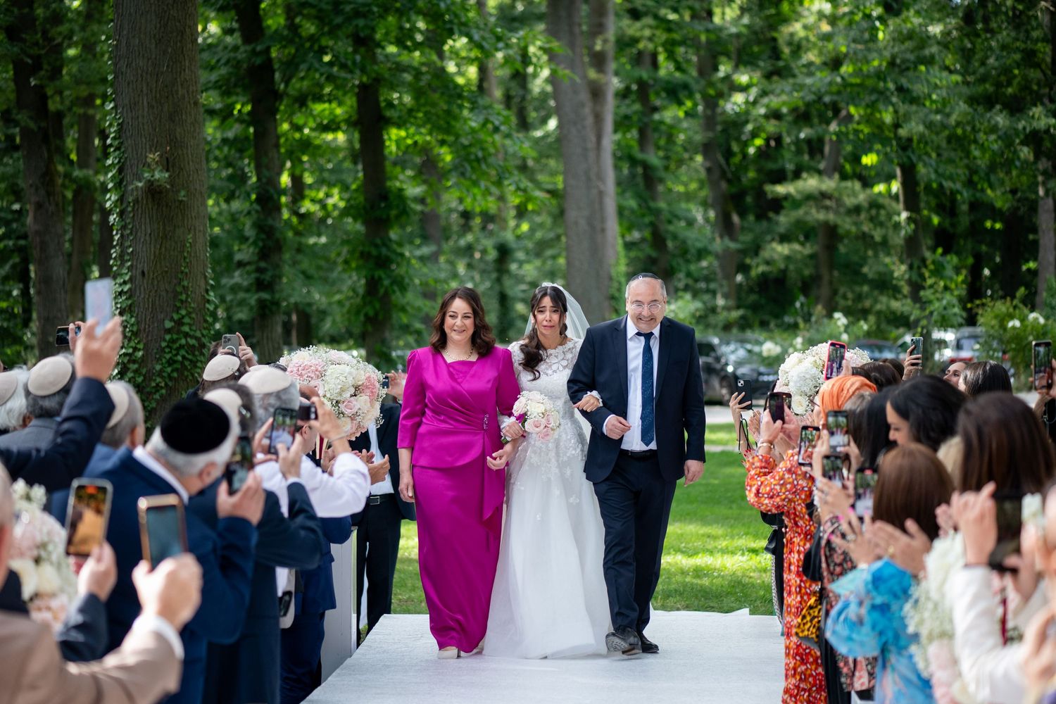 Entrée des mariés sous les applaudissements des invités, cérémonie de mariage en extérieur entourée d’arbres.