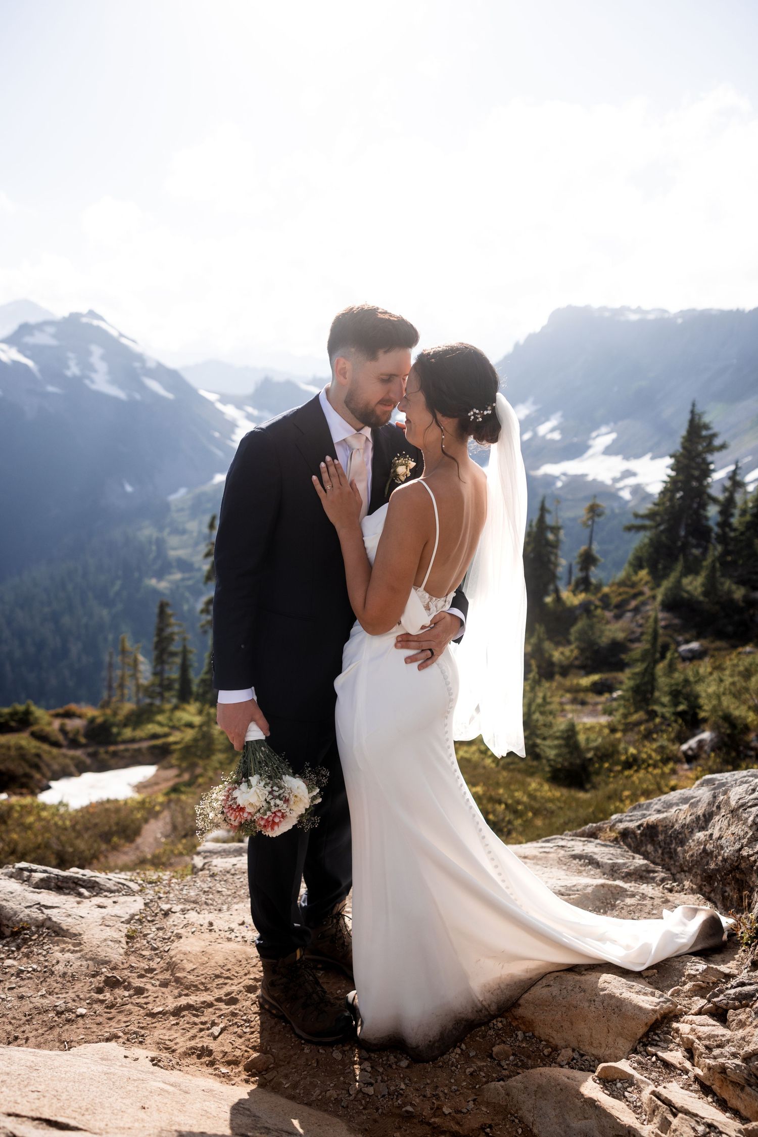 A romantic wedding photoshoot in a scenic mountain landscape with snow-capped peaks in the background.