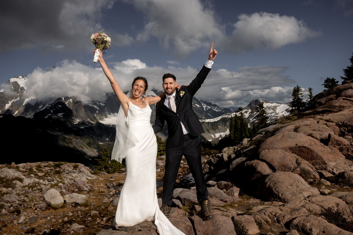 Celebratory wedding photos on mountain rocks with dramatic cloudy sky backdrop.
