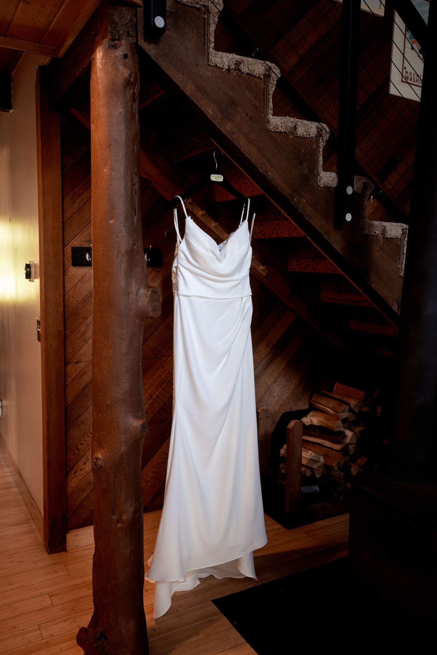 White wedding dress hanging elegantly from wooden beams in a rustic interior setting.