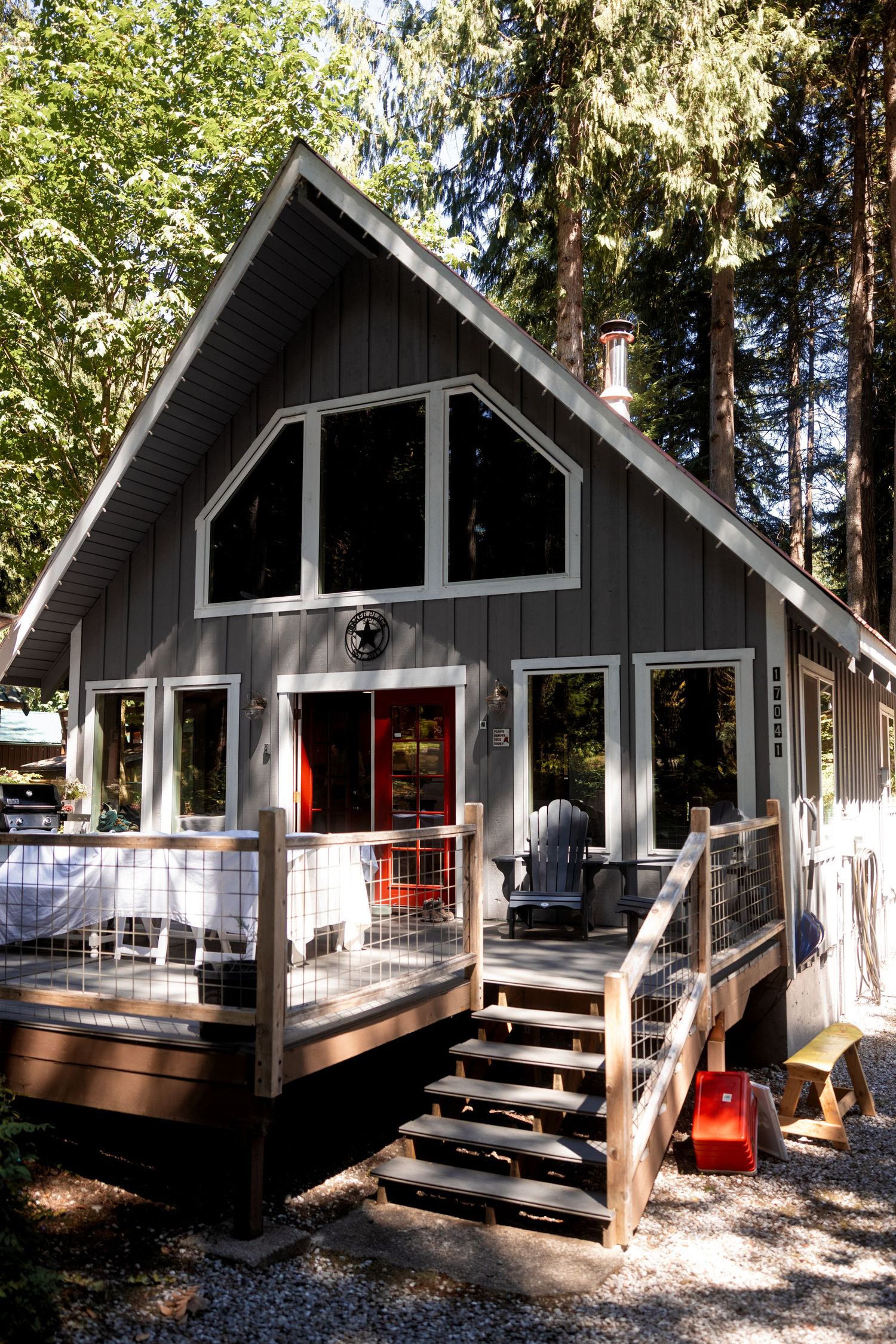 A series of views showing a modern gray A-frame cabin with red door and wooden deck nestled among tall pine trees.
