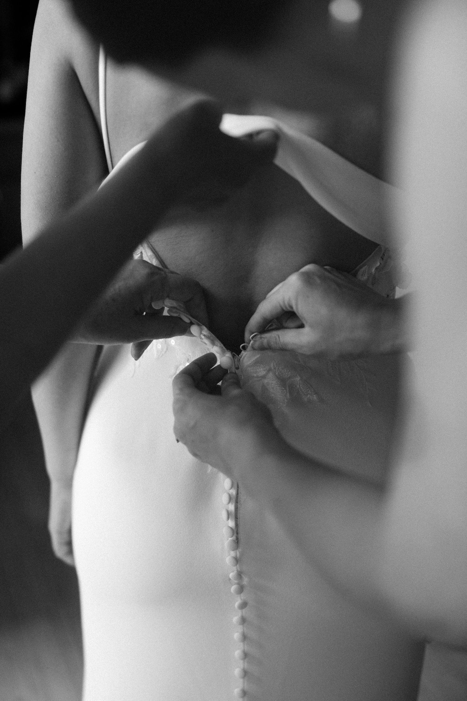 Black and white detail shot of buttons being fastened on a wedding dress.