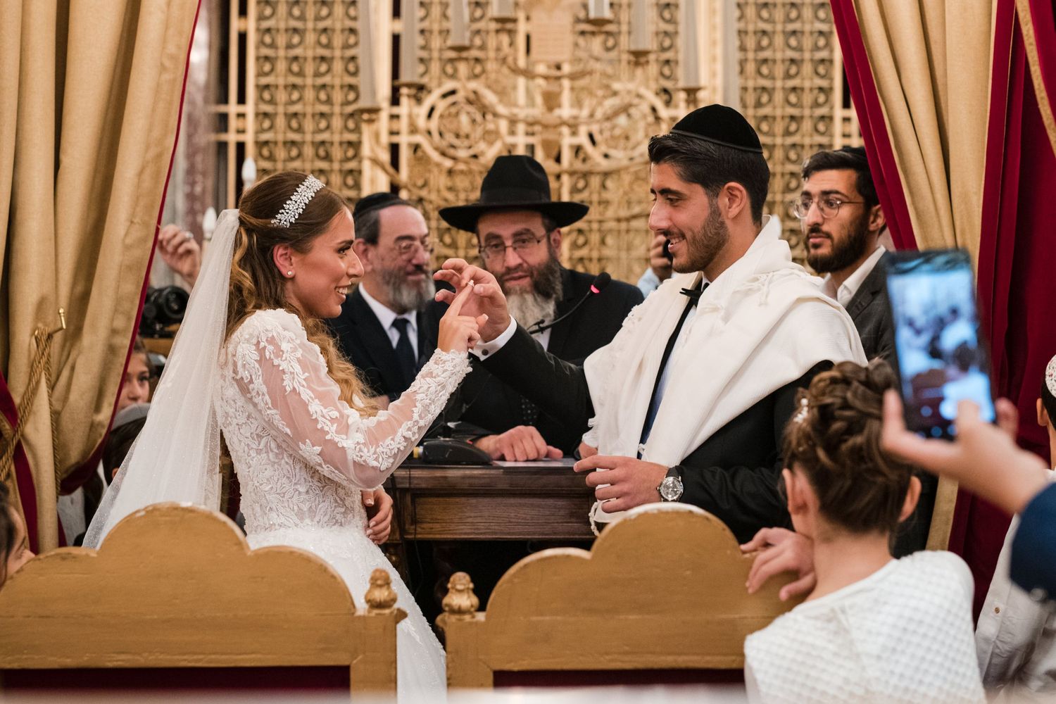 Remise de l'alliance sous la Houppa, mariés souriants et rabbin officiant lors d’un mariage juif traditionnel.