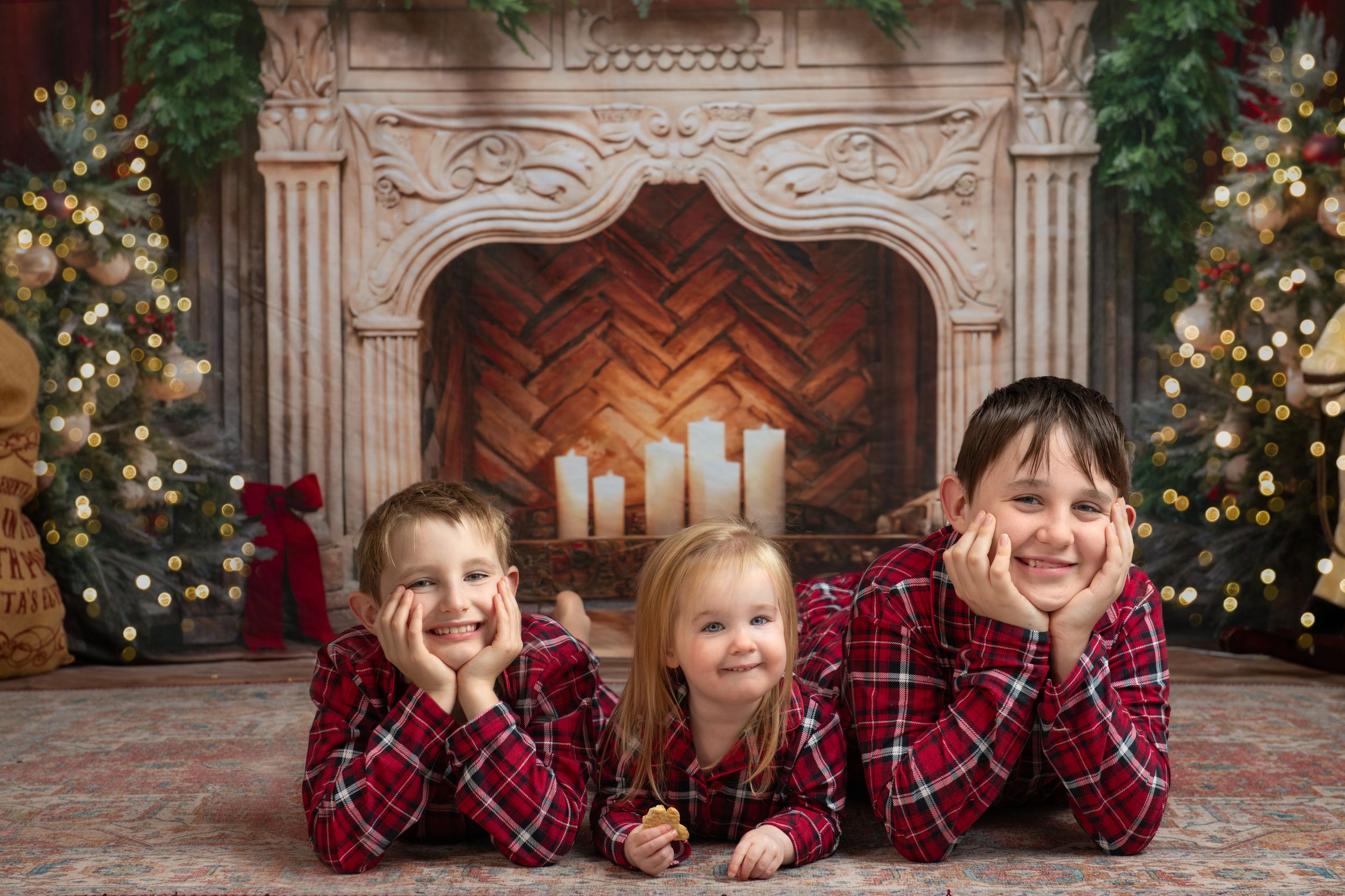 Children in matching red plaid outfits pose together in front of decorated Christmas trees and ornate stone fireplace.